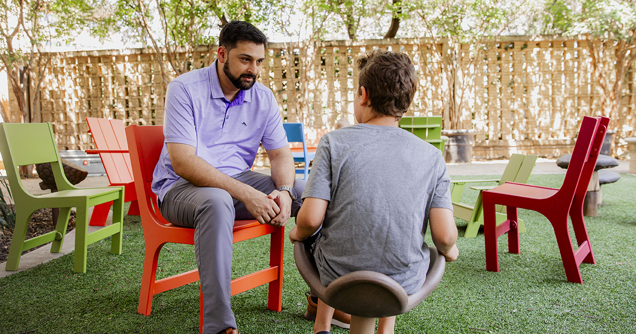Friendly mental health provider counsels a teenage boy in and outdoor sitting space..