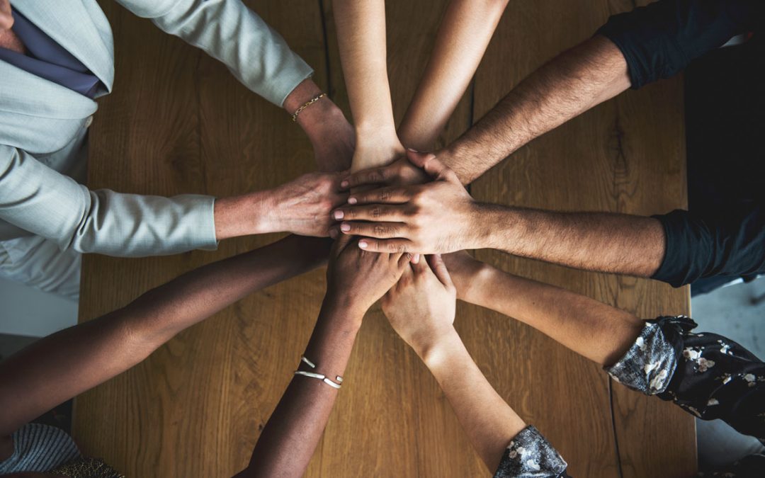 Several people placing hands together over a wooden table to represent teamwork