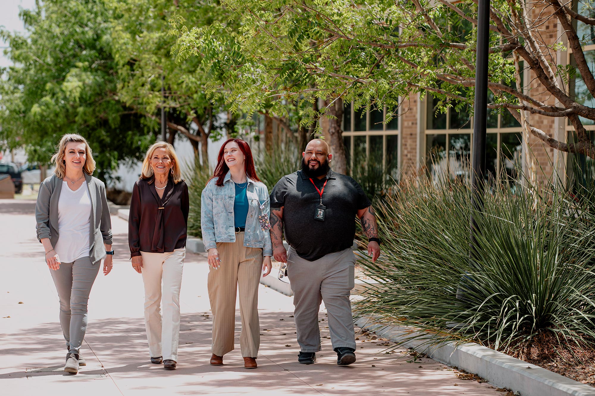 Four people walking together outside an office building along a landscaped sidewalk