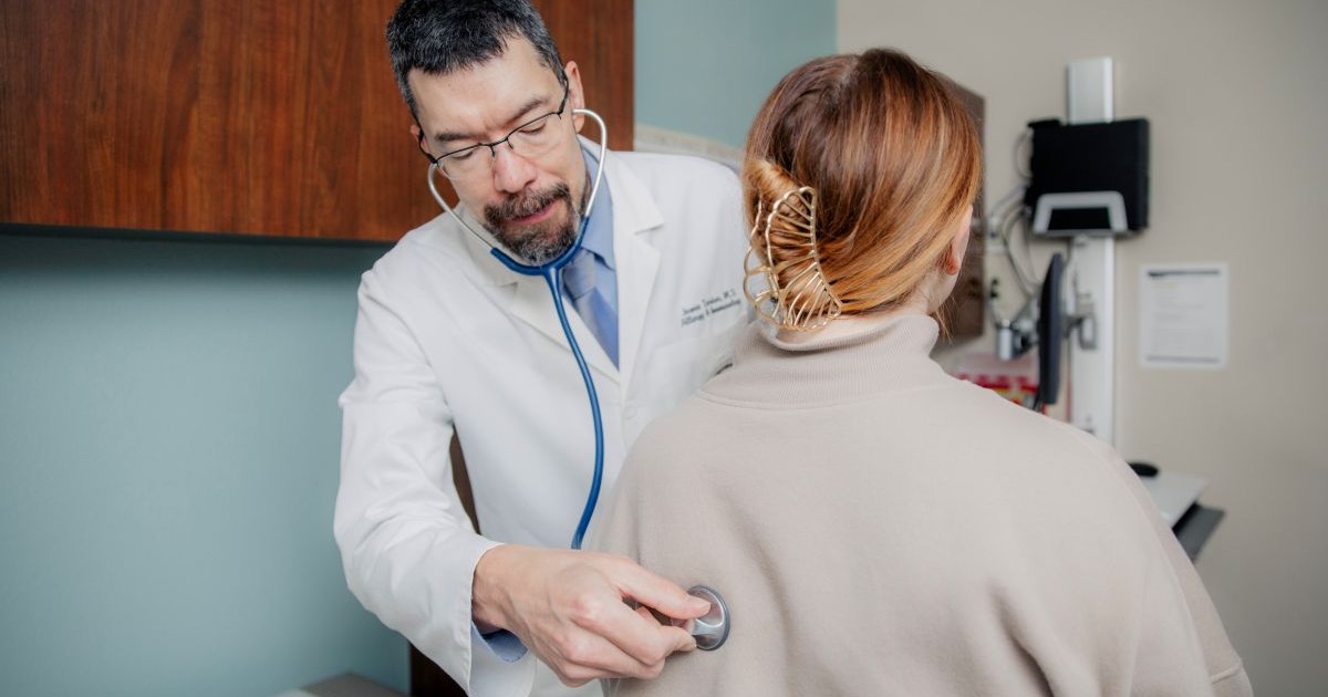 Doctor places stethoscope on patient's back