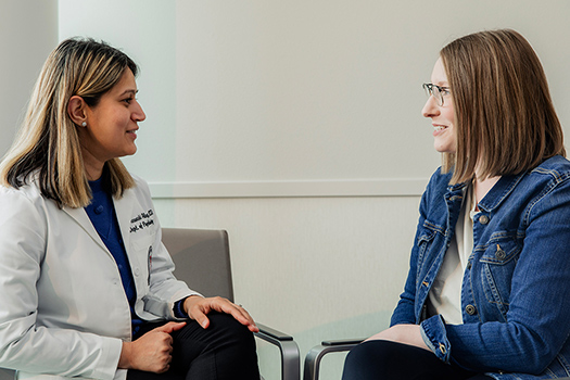 Provider sitting in front of patient in clinic room smiling, in conversation.