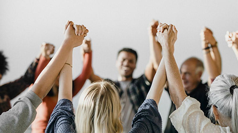 People in a circle holding hands in the air.